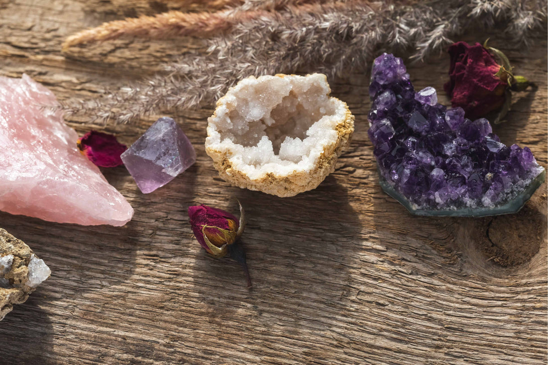 Photo d'une mini géode de cristal, d'une améthyste brute et d'une grosse pierre de quartz rose brute posés sur du bois.