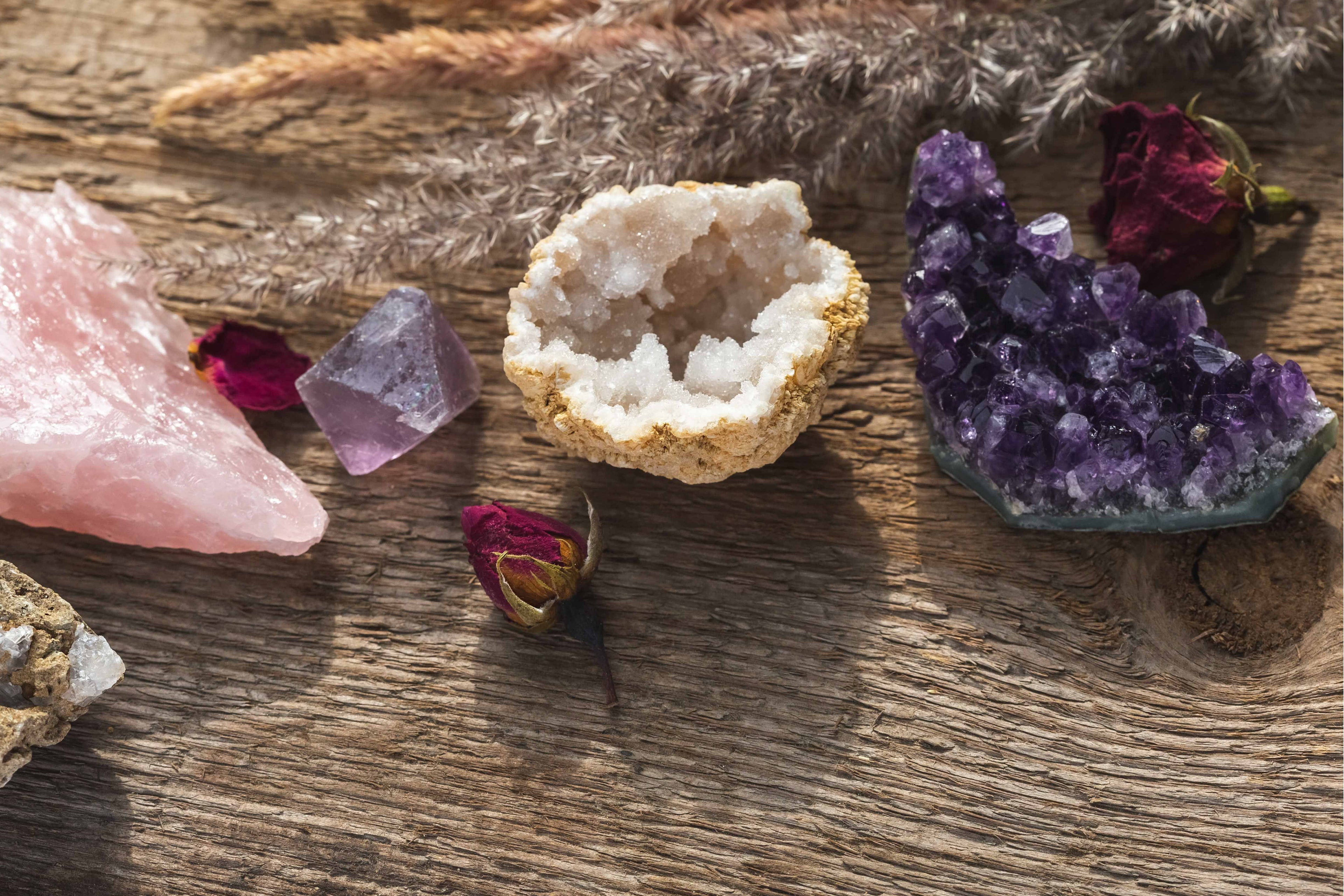 Photo d'une mini géode de cristal, d'une améthyste brute et d'une grosse pierre de quartz rose brute posés sur du bois.