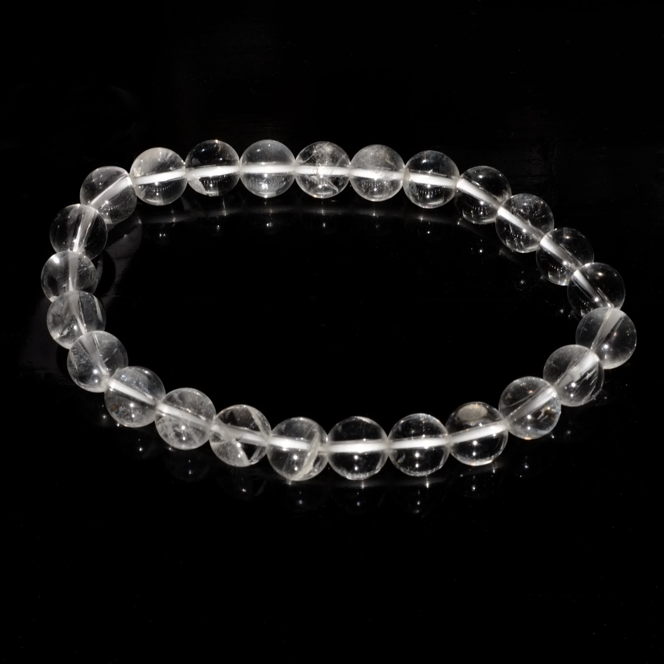 Bracelet boule en cristal de roche du Brésil sur fond noir éclairé par la lumière du soleil.